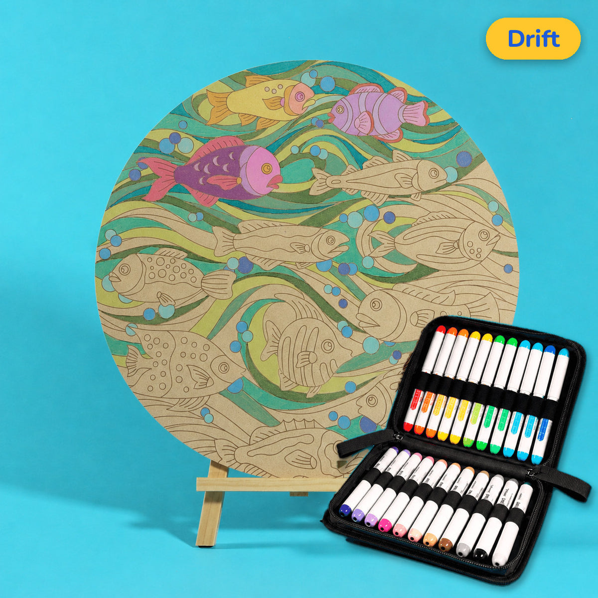 400mm Drift engraved circle art board with fish, flowing waves and bubbles, top coloured with pink fish and green waves, beside a case of 24 Nahuku markers