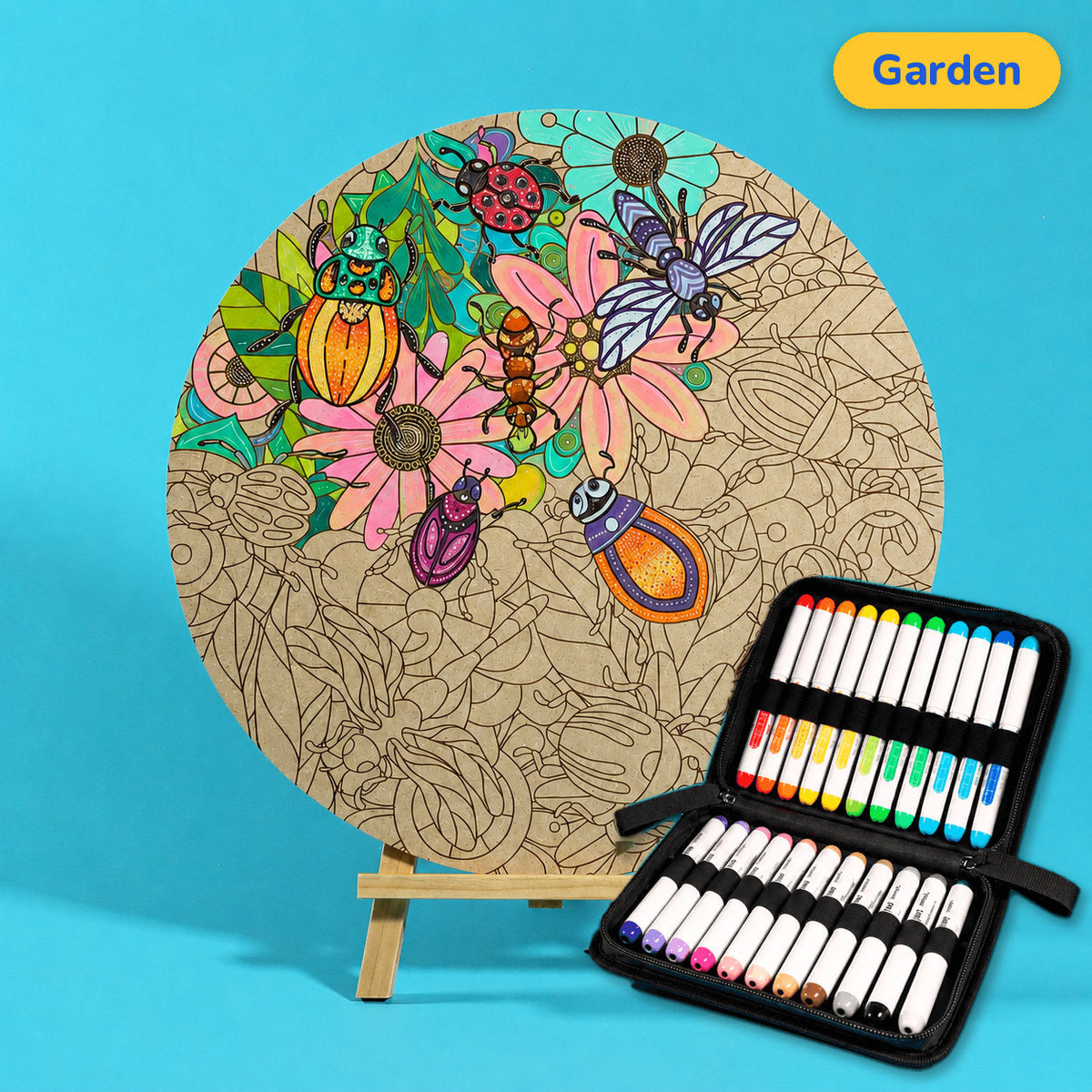 400mm Garden engraved circle art board with daisies, leaves, beetles and bees, top left coloured pink, green and orange, beside a case of 24 Nahuku markers