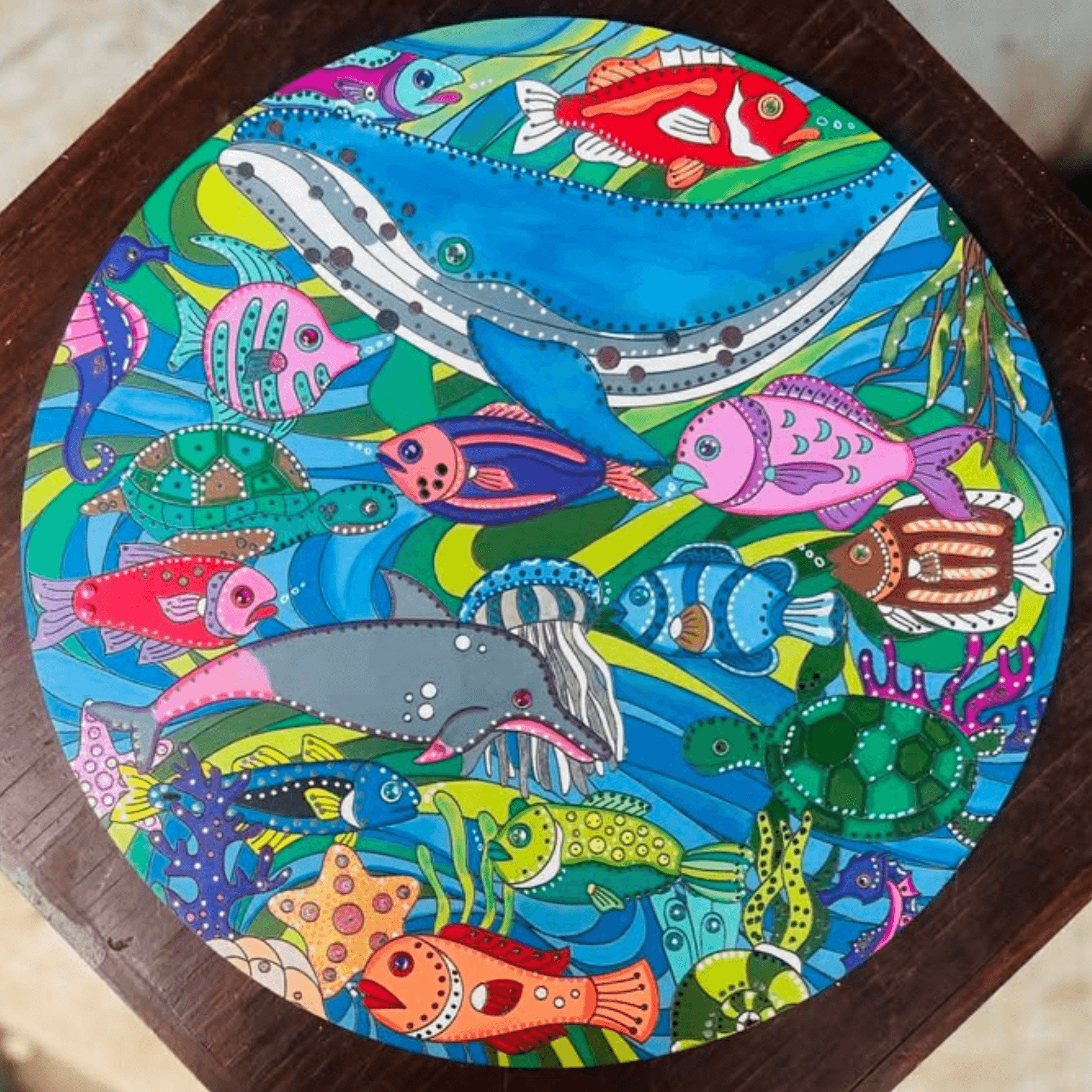 Colourful underwater scene with fish and whales on a circular wooden board.