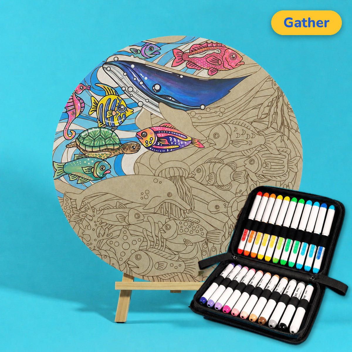 400mm Gather engraved circle art board with whales, turtles and fish, top left coloured with a blue whale and bright fish, beside a case of 24 Nahuku markers