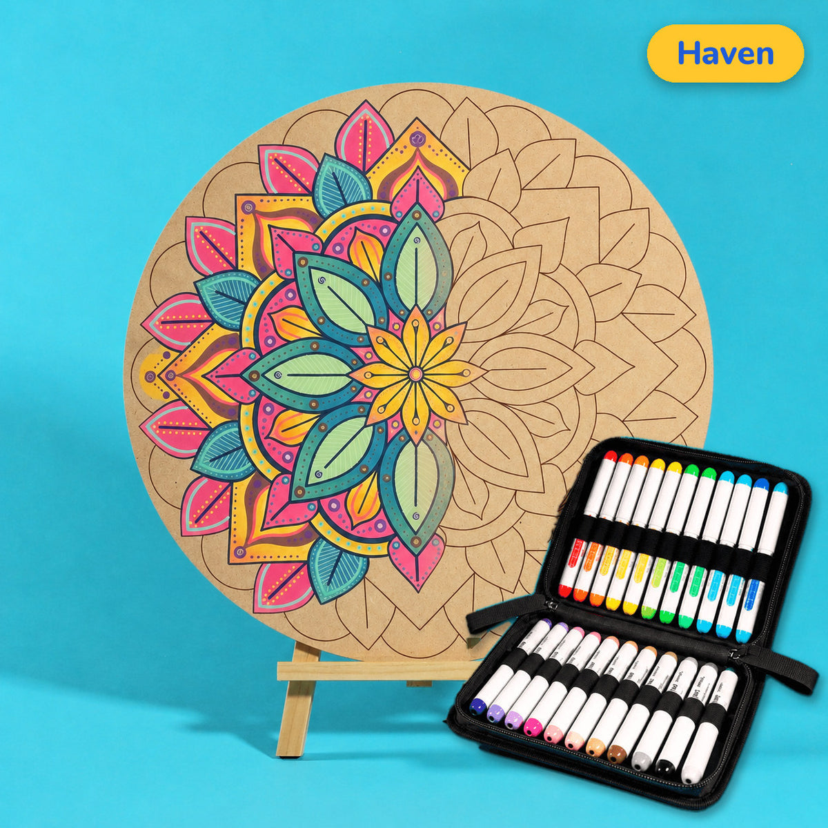 400mm Haven engraved circle art board with mandala of overlapping leaves, left half coloured pink, teal and yellow, beside a case of 24 Nahuku markers