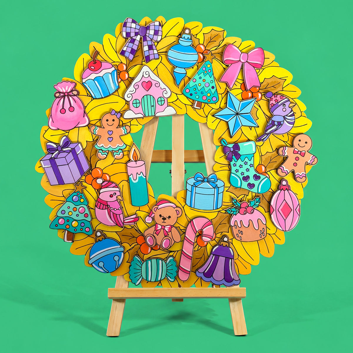 Jingle Jumble Christmas Wreath by Hueray, a yellow MDF leaf wreath with 24 coloured press-out ornaments, displayed on a wooden easel on a green background
