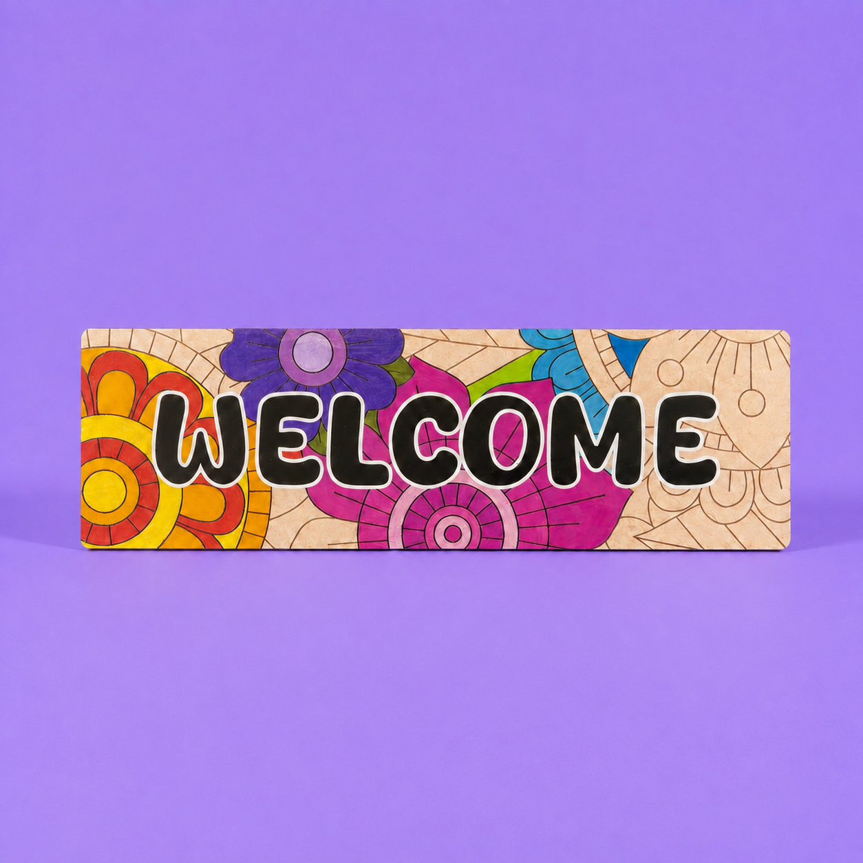 A rectangular decorative sign with the word “WELCOME” in large black letters over a colorful floral and geometric pattern, photographed against a solid purple background.