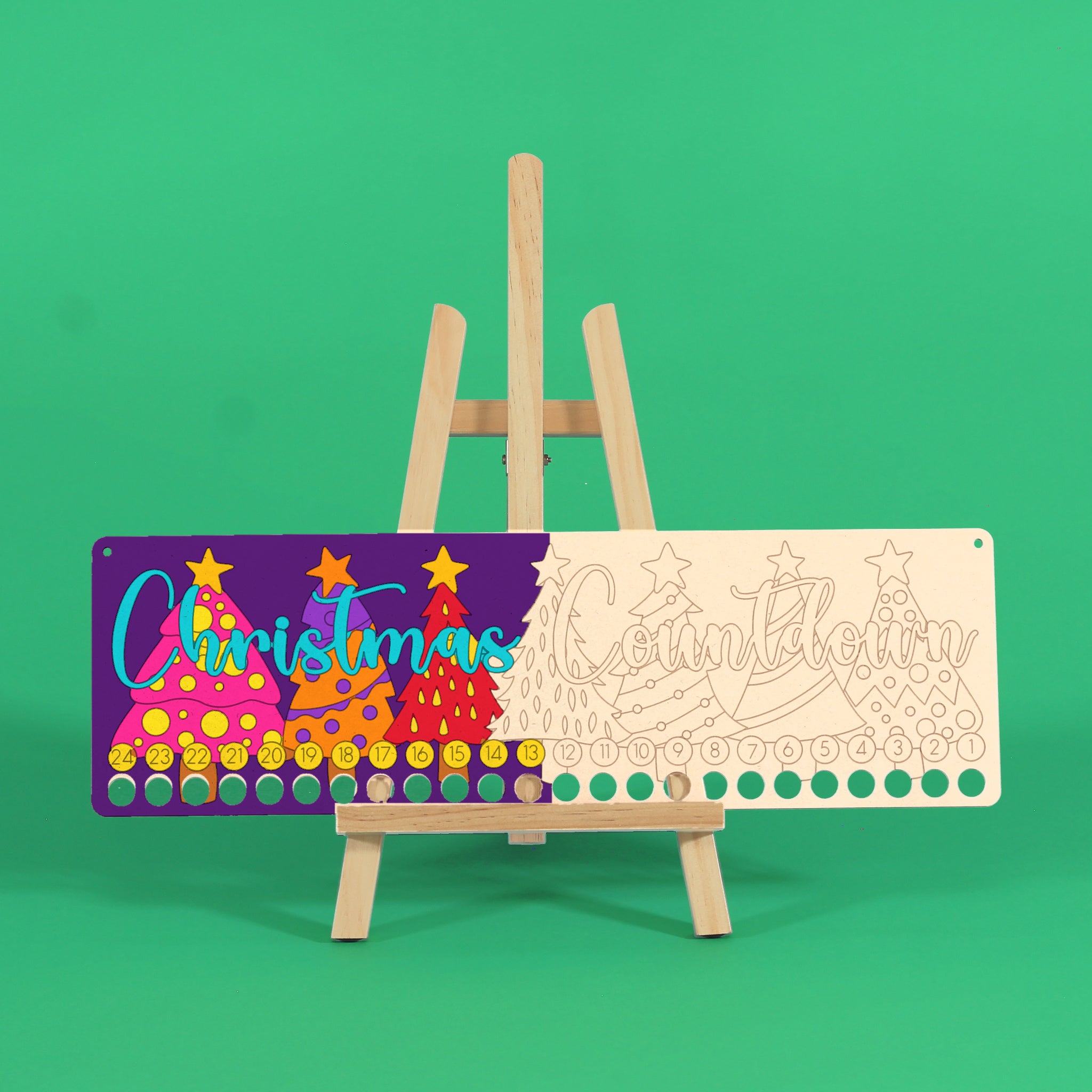Partly coloured Christmas Countdown art board on a wooden easel against a green background, with brightly painted Christmas trees on the left and uncoloured engraved trees on the right