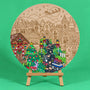 Mistletoe Lane 400mm round Christmas art board on an easel, partly coloured, with storybook houses, a Christmas tree, a deer, a rabbit and Santa's sleigh over the moon