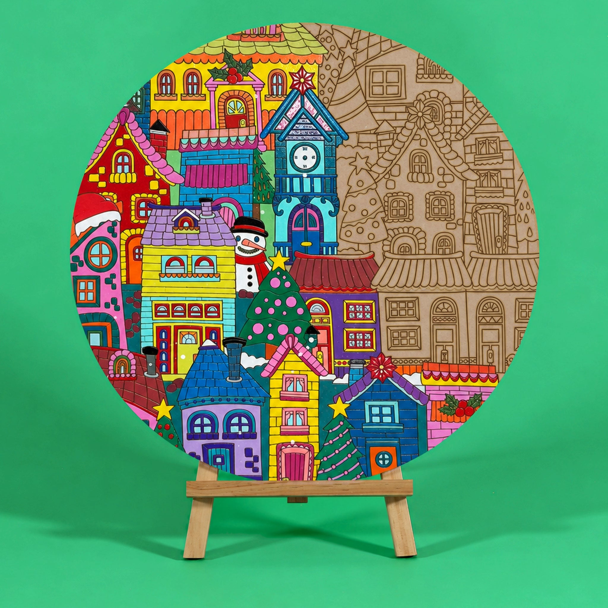 Twinkle Town 400mm round Christmas art board on an easel, half coloured in rainbow shades, showing village houses, a clock tower and Christmas trees
